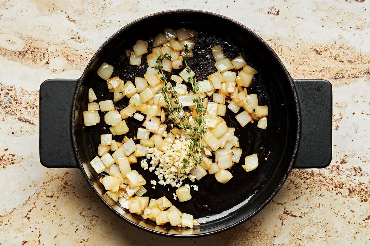 onion, garlic and thyme being cooked in olive oil in a skillet
