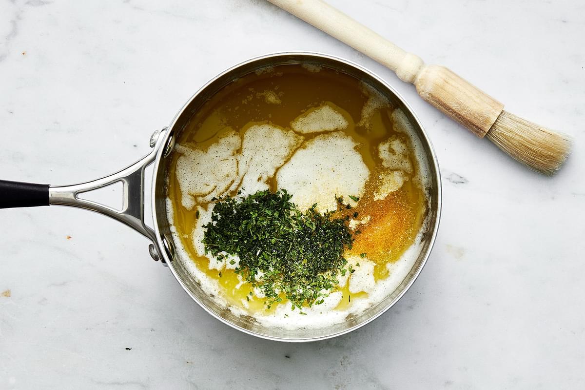 a pot with melted butter, salt, parsley, onion and garlic powders next to a pastry brush on the counter