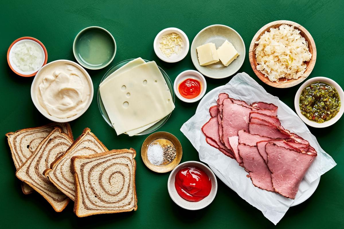 rye bread, pastrami, sauerkraut kraut, Swiss cheese and ingredients for Russian style dressing on the counter for reubens