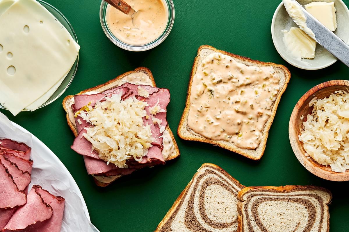 reuben sandwiches being assembled made with rye bread, pastrami, sauerkraut, Swiss cheese and Russian style dressing