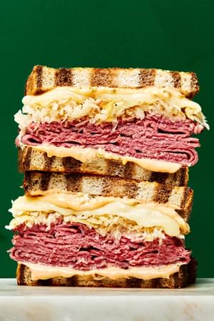 a stacked reuben sandwich made with rye bread pastrami, sauerkraut, Swiss cheese & Russian  style dressing
