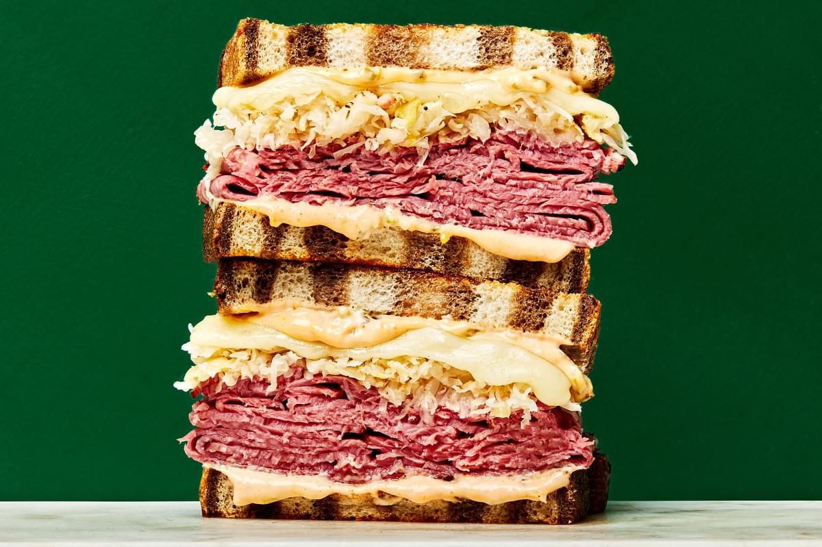 a reuben sandwich cut in half and stacked on top of each other made with pastrami, sauerkraut, Swiss cheese& Russian dressing