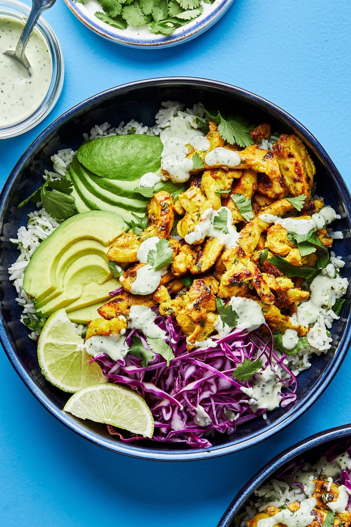 A rice bowl with turmeric ginger chicken, avocado, red cabbage, lime wedges and cilantro ranch