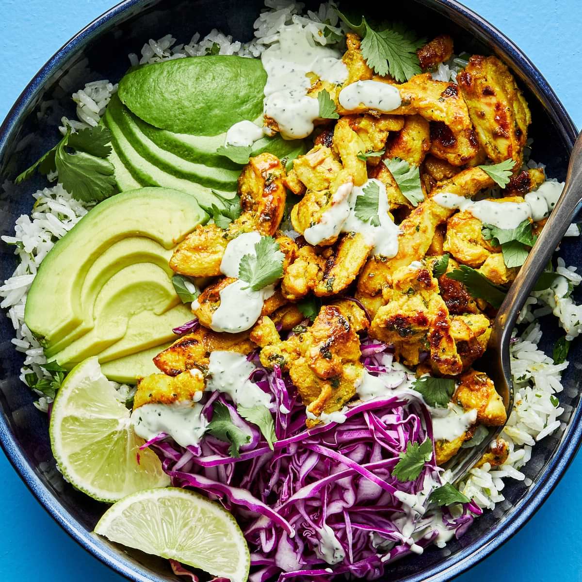 A rice bowl with turmeric ginger chicken, avocado, red cabbage, lime wedges and cilantro ranch