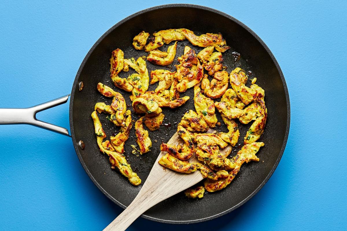 turmeric ginger chicken being cooked in a skillet with a wooden spoon