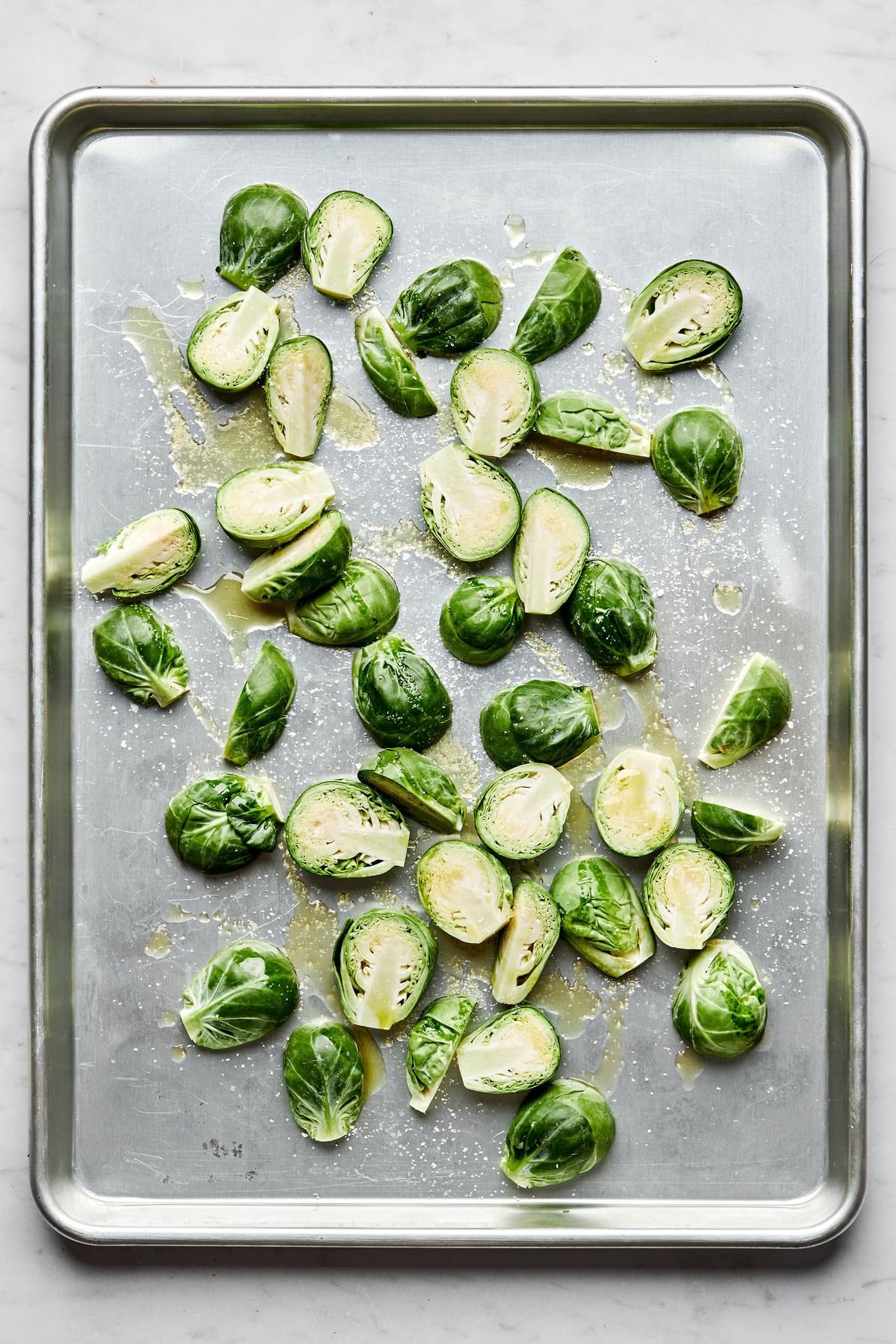 raw Brussels sprouts cut in half tossed in olive oil and salt on a baking sheet ready to be roasted in the oven