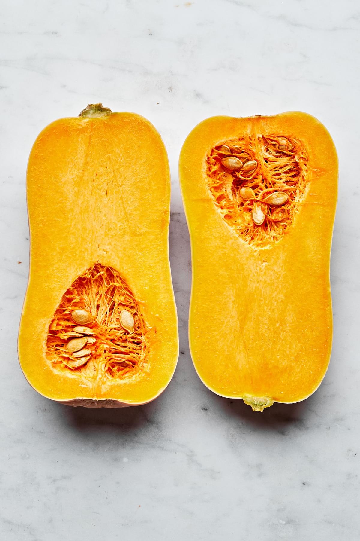 a raw butternut squash cut in half lengthwise on the counter