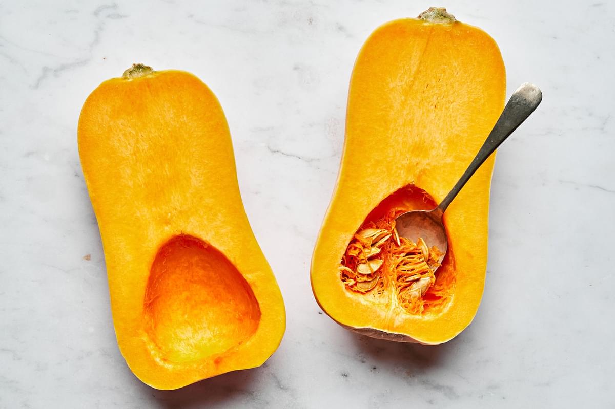 seeds being scooped out of a a raw, peeled butternut squash that has been cut in half length wise