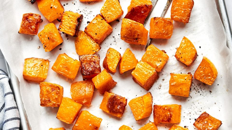cubed roasted butternut squash seasoned with olive oil, salt and pepper on a baking sheet with a serving fork