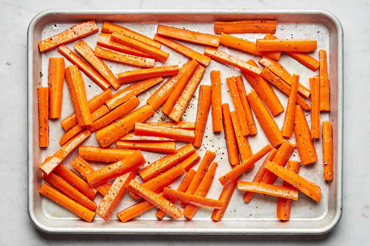 raw carrots tossed with olive oil, salt, pepper and garlic powder on a baking sheet ready to be baked