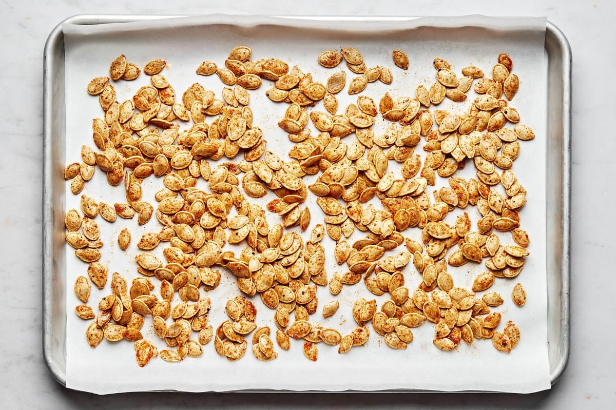 raw pumpkins seeds on a parchment lined baking sheet ready to be roasted tossed with vegetable oil and seasonings