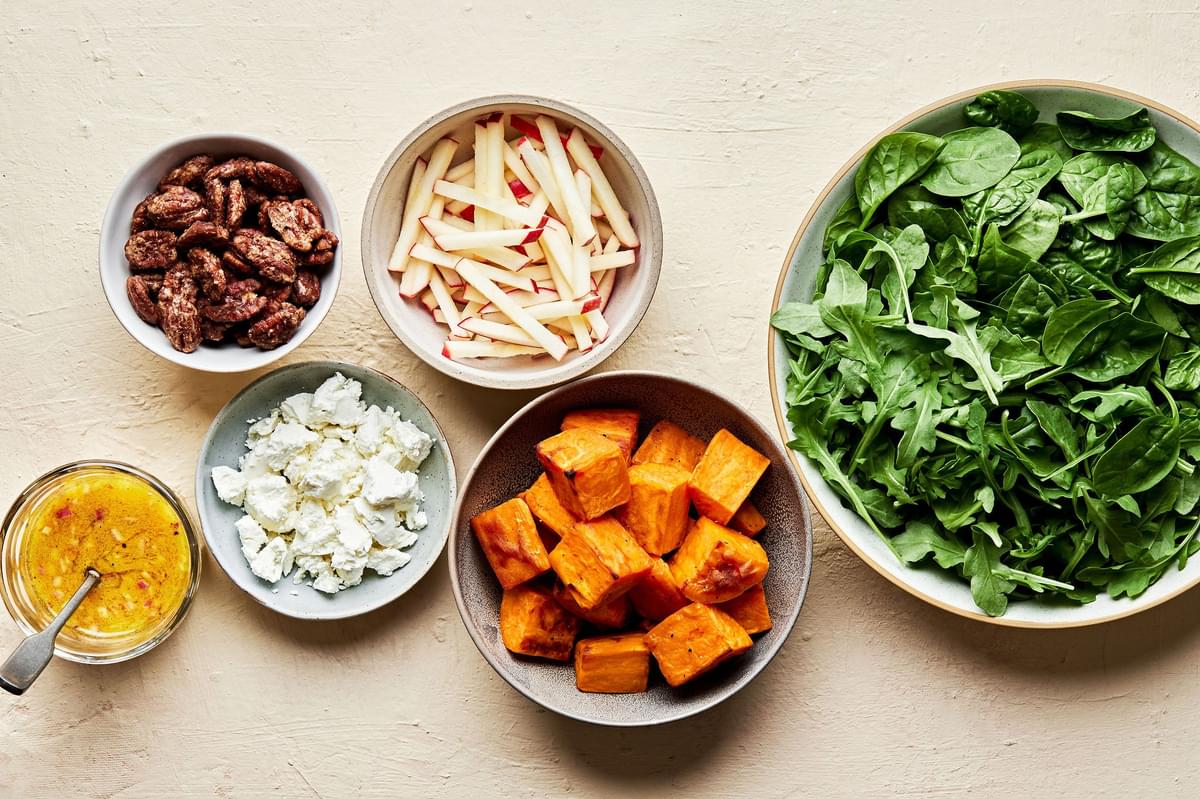 arugula, spinach, roasted sweet potatoes, candied pecans, goat cheese, apples & orange vinaigrette in bowls on the counter