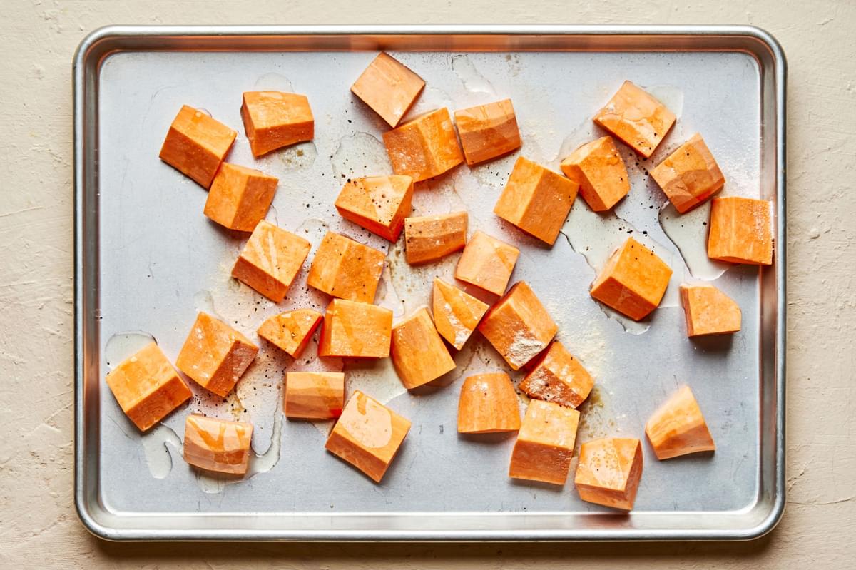 chopped sweet potatoes tossed with olive oil, salt, garlic powder & pepper on a baking sheet ready to be roasted in the oven