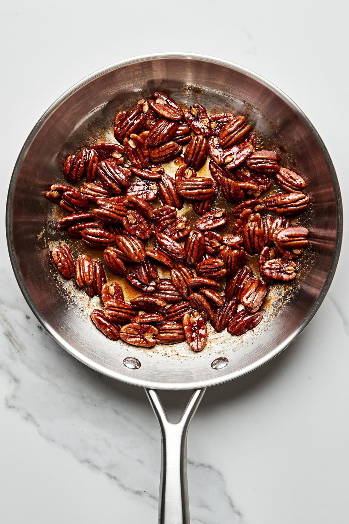 pecans being candied in a skillet with brown sugar, cinnamon, salt, and cayenne