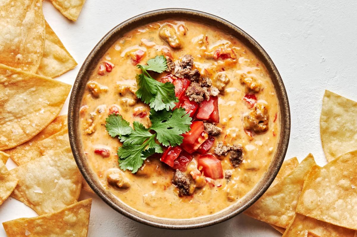 a bowl of rotel dip topped with cilantro and tomatoes served with tortilla chips