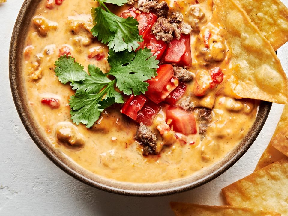 a bowl of rotel dip topped with cilantro and tomatoes served with tortilla chips