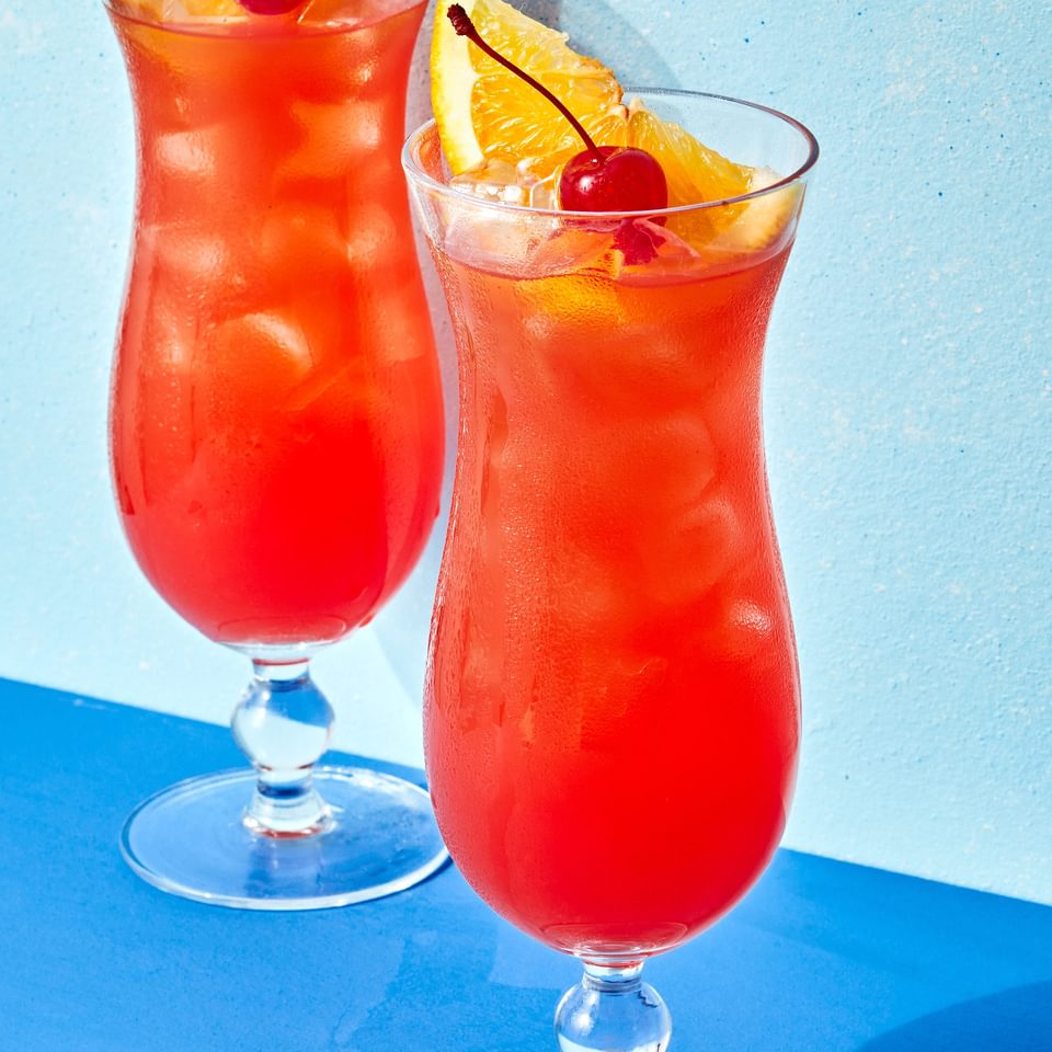 Rum punch in two tall glasses topped with cherries and a slice of orange.