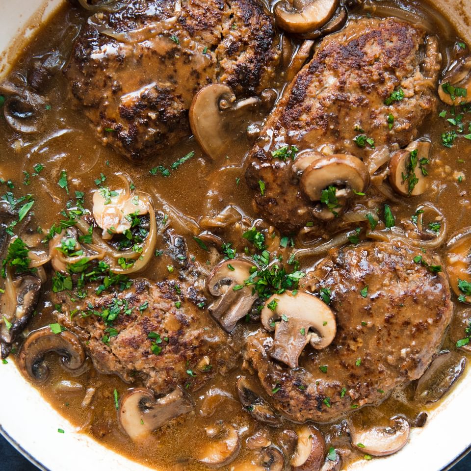 homemade Salisbury steak and gravy with mushrooms in a pot topped with fresh parsley