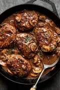 5 salisbury steaks in a homemade gravy with mushrooms and onions topped with fresh parsley in a cast iron skillet with spoon