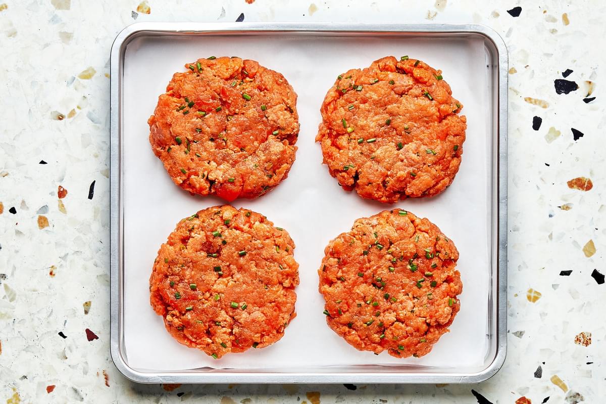 homemade salmon burger patties on a parchment paper lined baking sheet on the counter