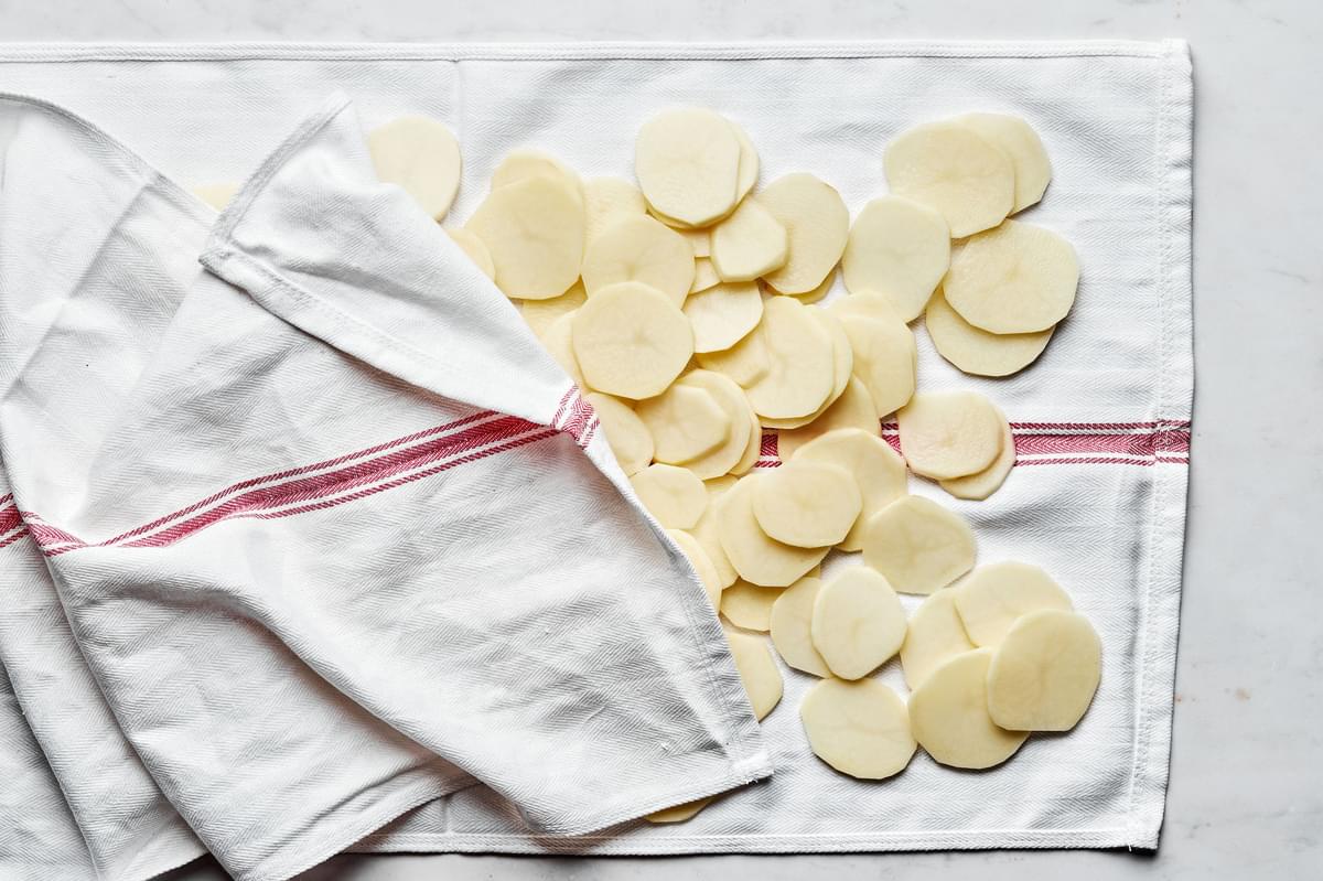 peeled, sliced and rinsed potatoes being patted dry on a kitchen towel