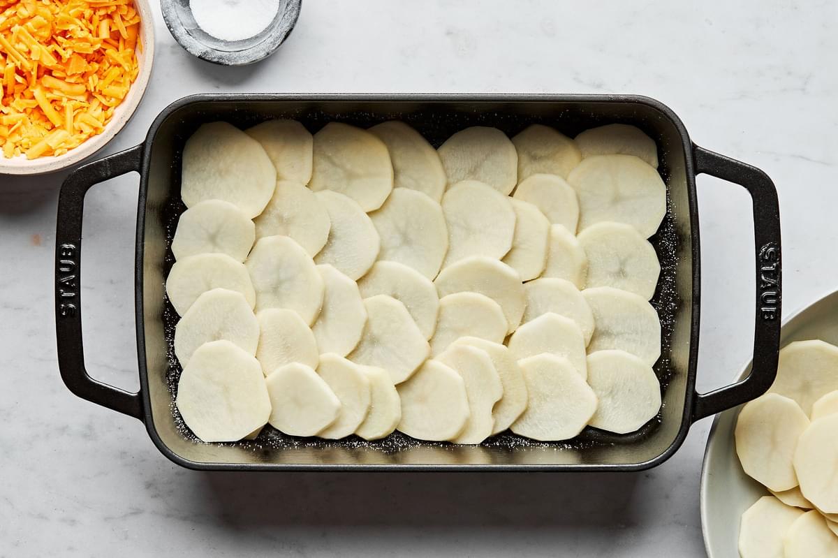 sliced potatoes layered on the bottom of a greased casserole dish