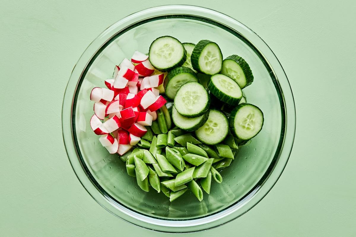 sliced snap peas, cucumbers and radishes in a glass bowl to make cucumber salad