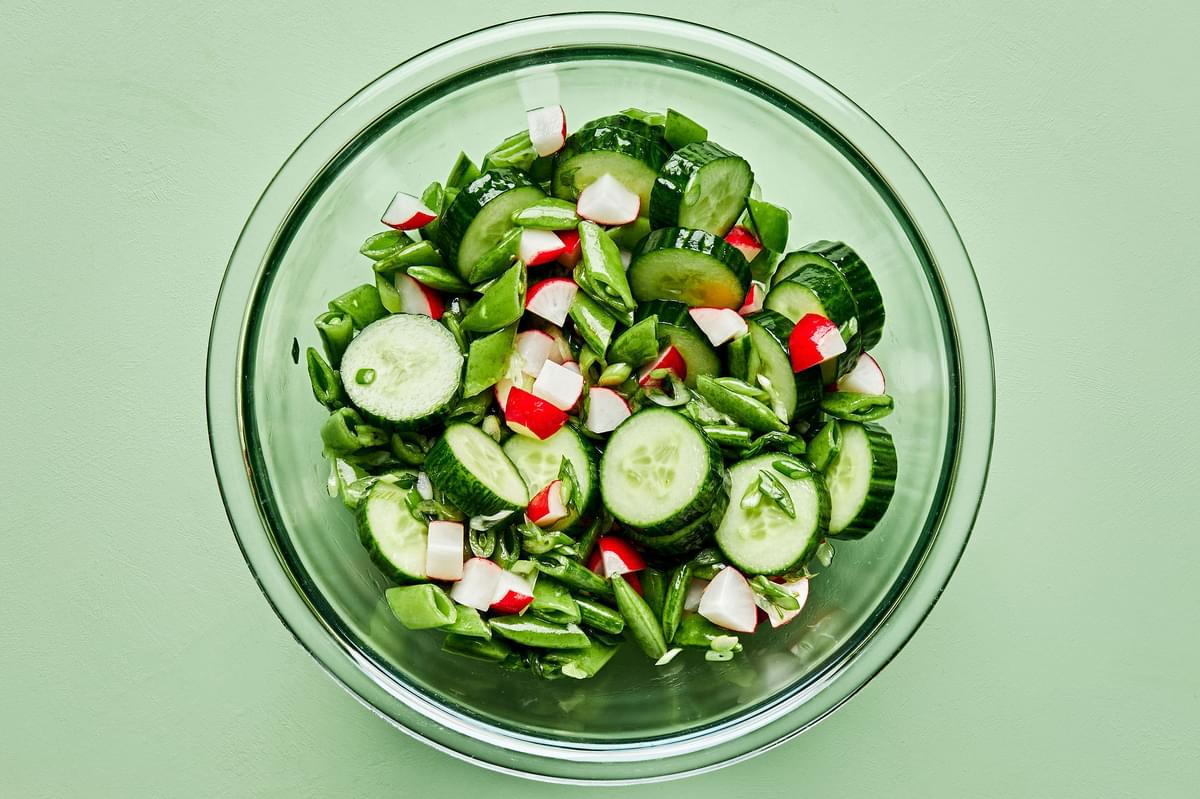 cucumber salad in a glass bowl made with cucumber, radish, snap peas, rice vinegar, sugar, salt sesame oil and green onions