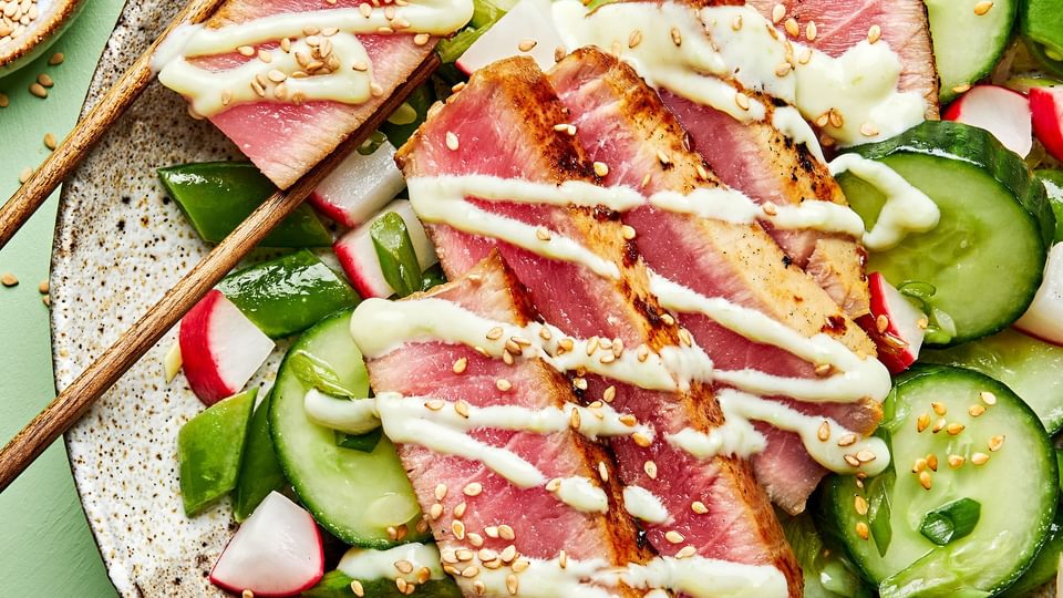 seared ahi tuna served on top of cucumber salad drizzled with  wasabi mayo and sprinkled with sesame seeds