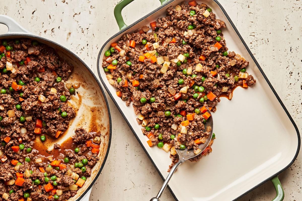 ground beef and vegetable mixture for shepherd's pie being spooned into a 9 x 13 casserole dish
