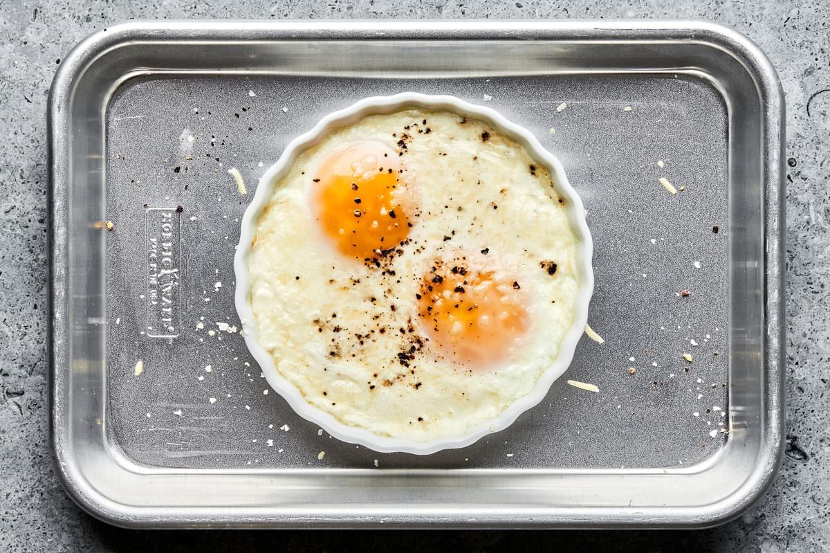 baked shirred eggs in a ramekin on top of a baking sheet. seasoned with salt and pepper and sprinkled with parmesan