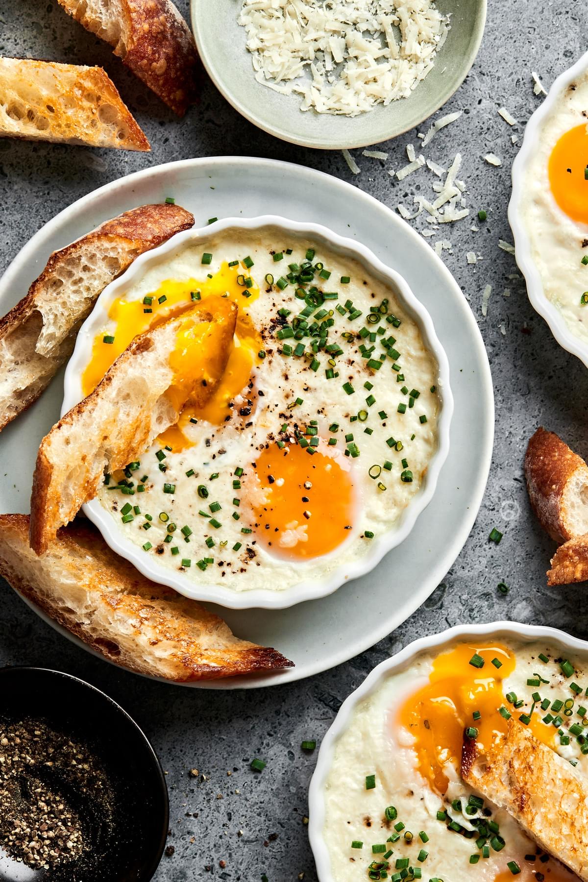 2 ramekins of shirred eggs garnished with chopped chives and served with crusty bread