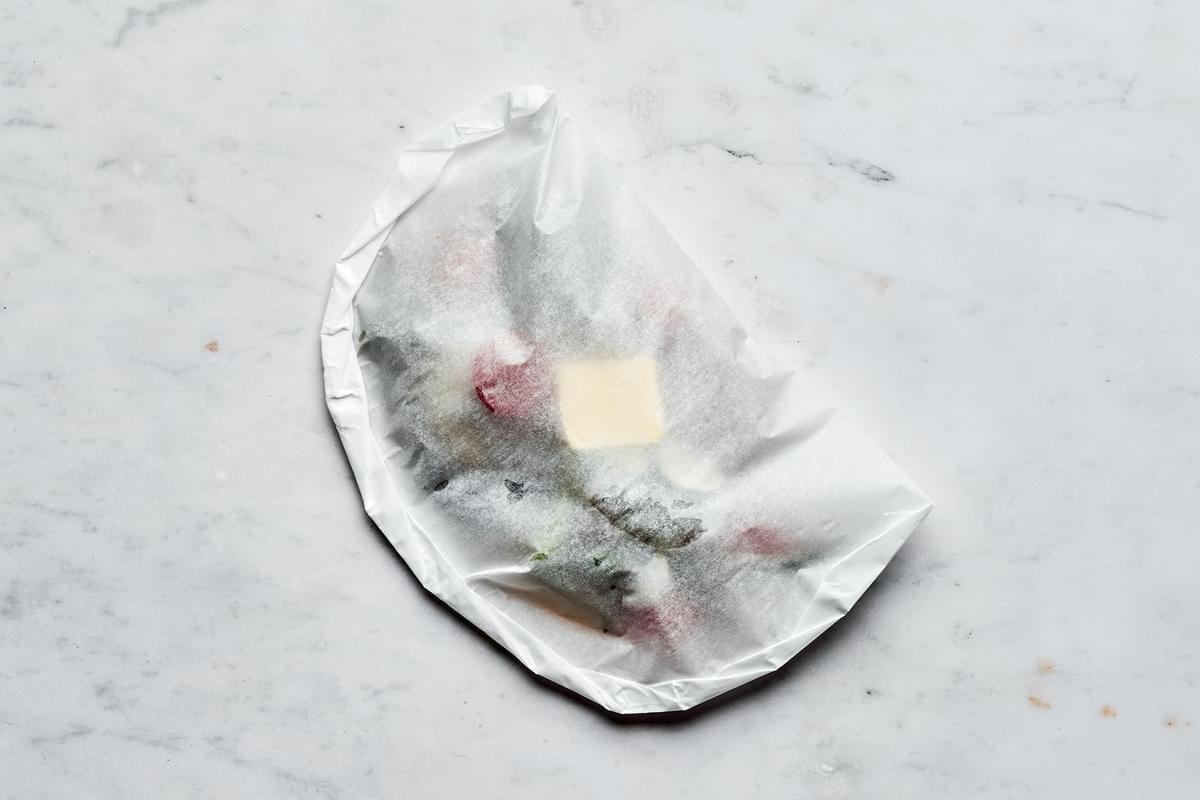 parchment paper being folded around the shrimp scampi with the edges firmly rolled to create sealed envelope for the scampi