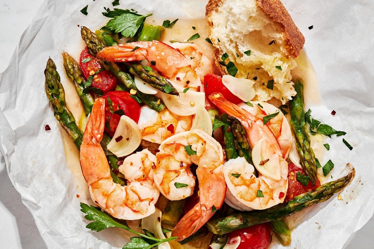 an opened Shrimp Scampi En Papillote filled with shrimp, asparagus, tomatoes and scampi sauce sprinkled with fresh parsley