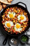 Homemade smoky bacon cheddar breakfast hash in a skillet topped with fried eggs.