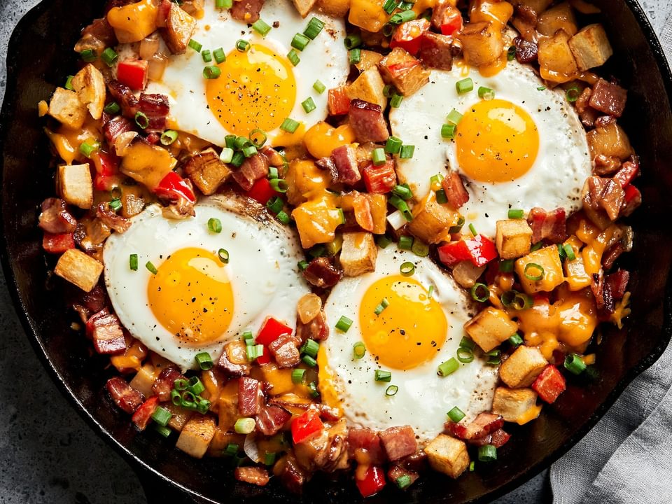 Homemade smoky bacon cheddar breakfast hash in a skillet topped with fried eggs.