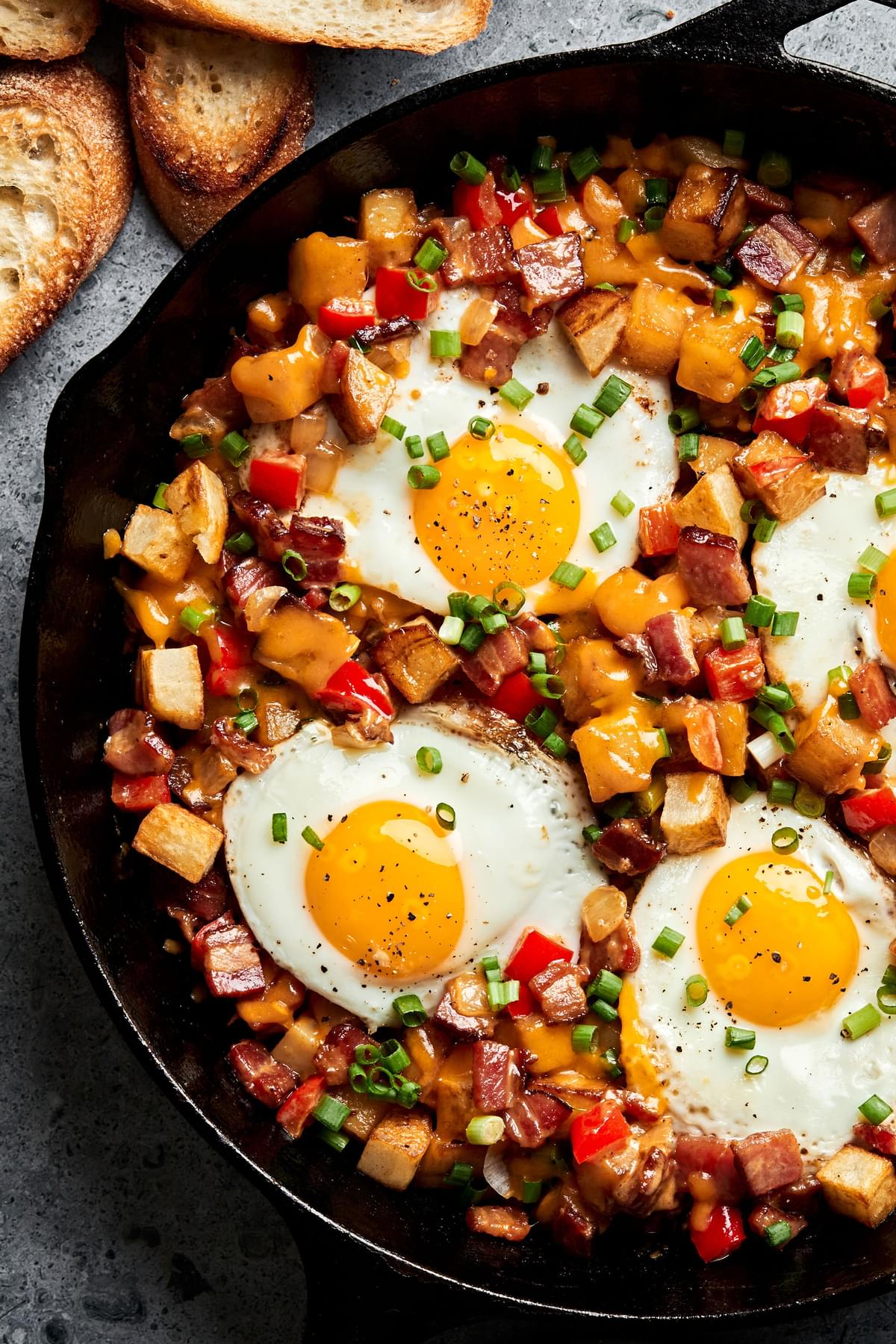 Smoky bacon cheddar breakfast hash topped with fried eggs in a skillet