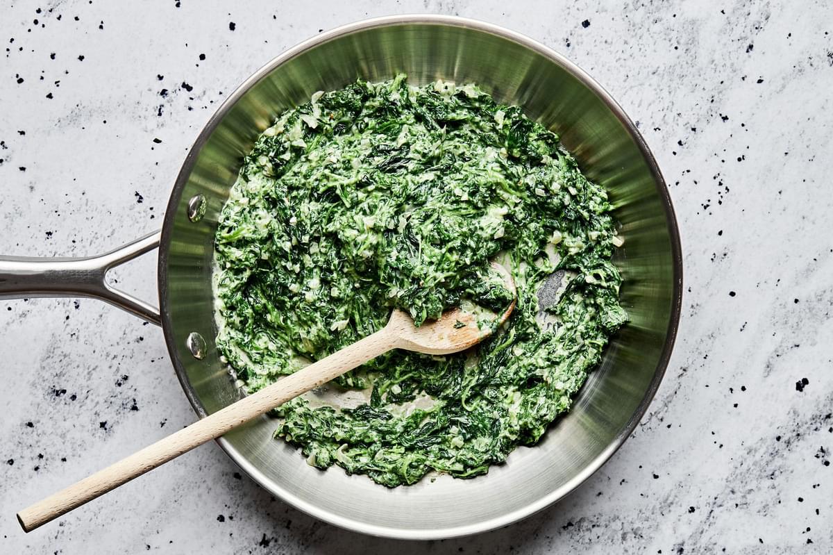 creamed spinach in a skillet made with butter, shallot garlic, heavy cream, mustard, spices, basil and parmesan