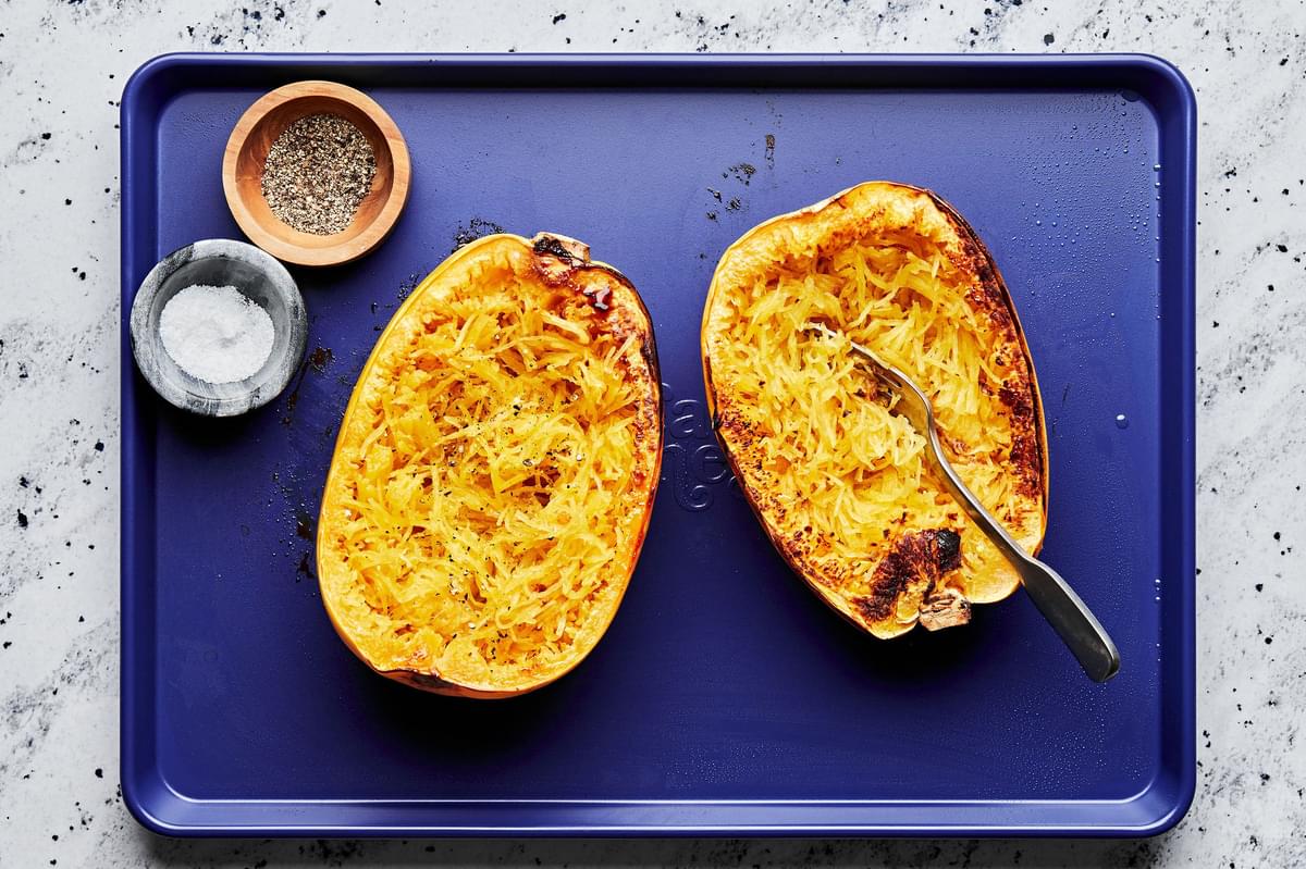 roasted spaghetti squash being scooped out of the skins on a baking sheet next to salt and pepper