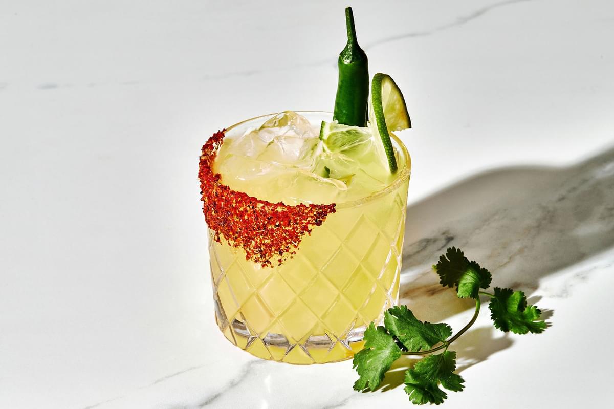 A spicy margarita with juicy lime, tequila, a hint of serrano Chile with a Tajin seasoning rim and a lime and Serrano garnish