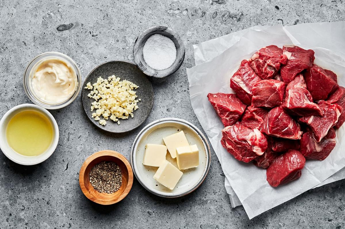 sirloin steak, olive oil, salt, butter, garlic cloves, and pepper in bowls to make steak bites