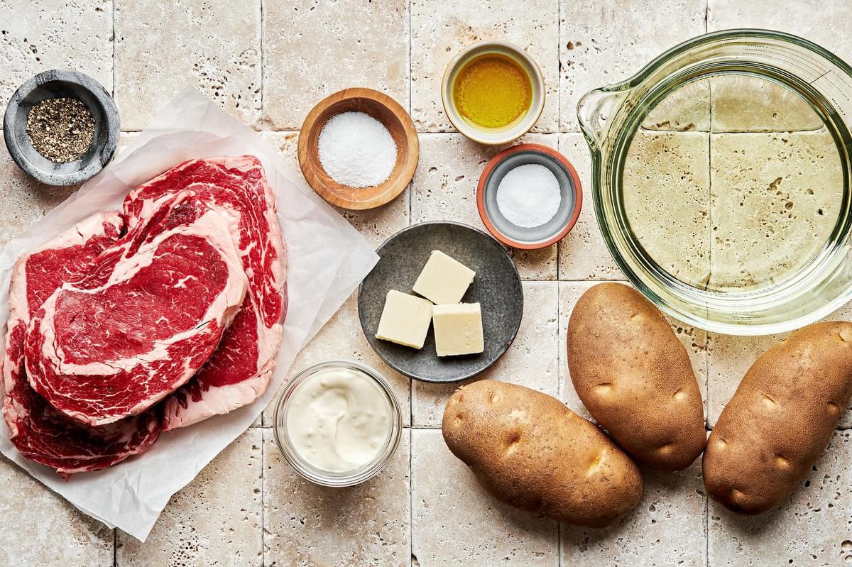 ribeye steak, russet potatoes, peanut oil, olive oil, salt, butter, pepper and garlic aioli in bowls to make Steak Frites