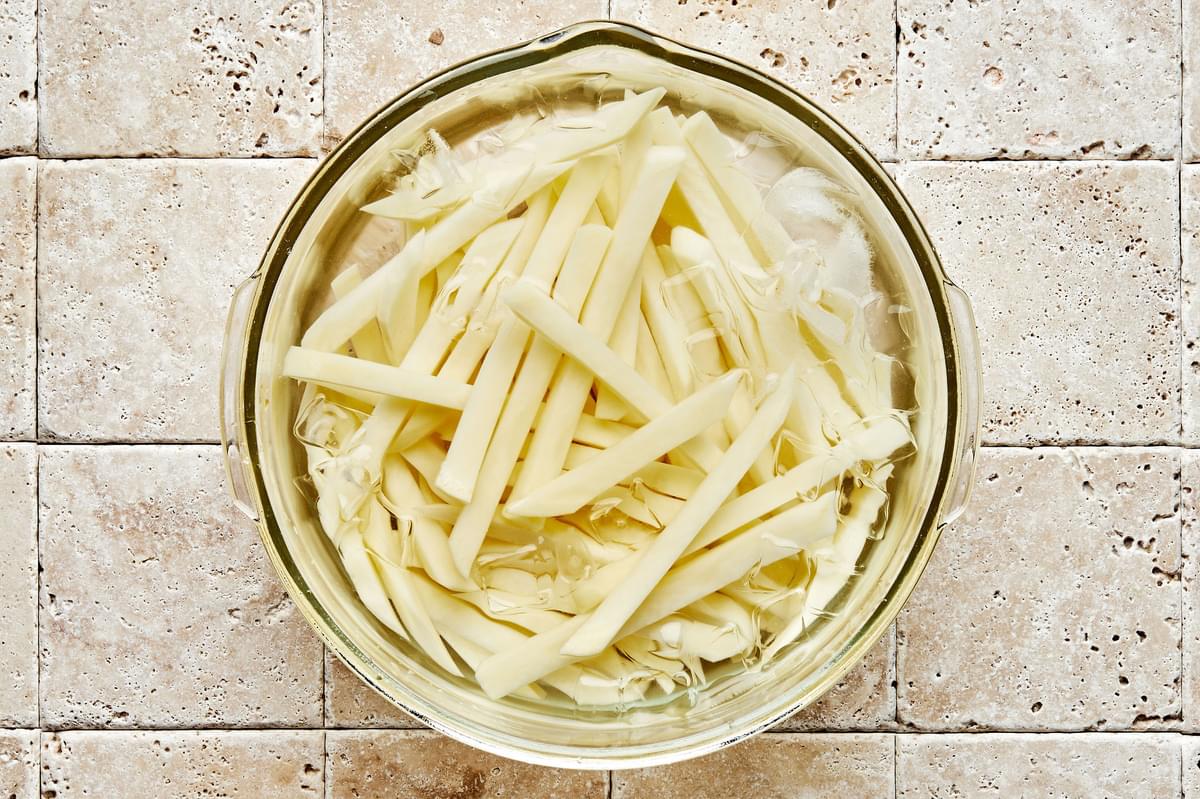 potatoes sliced into French fries soaking in a bowl of ice water to remove starch before frying