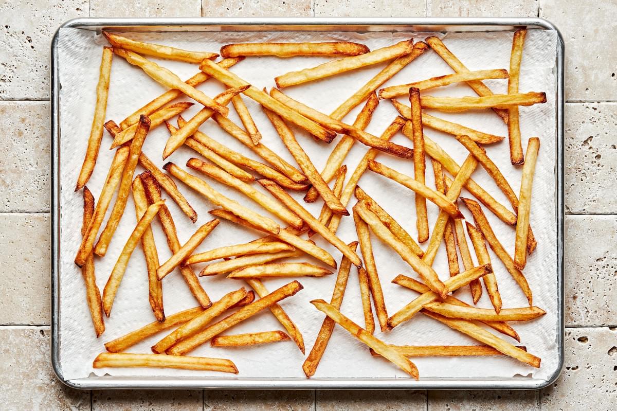 homemade French fries cooling on a paper towel lined baking sheet after being fried two times