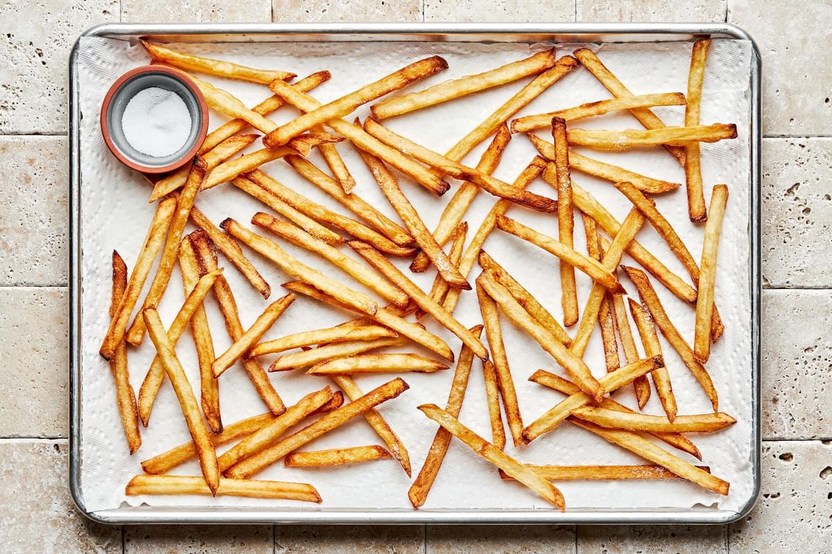 homemade French fries cooling on a paper towel lined baking sheet and seasoned with salt and pepper