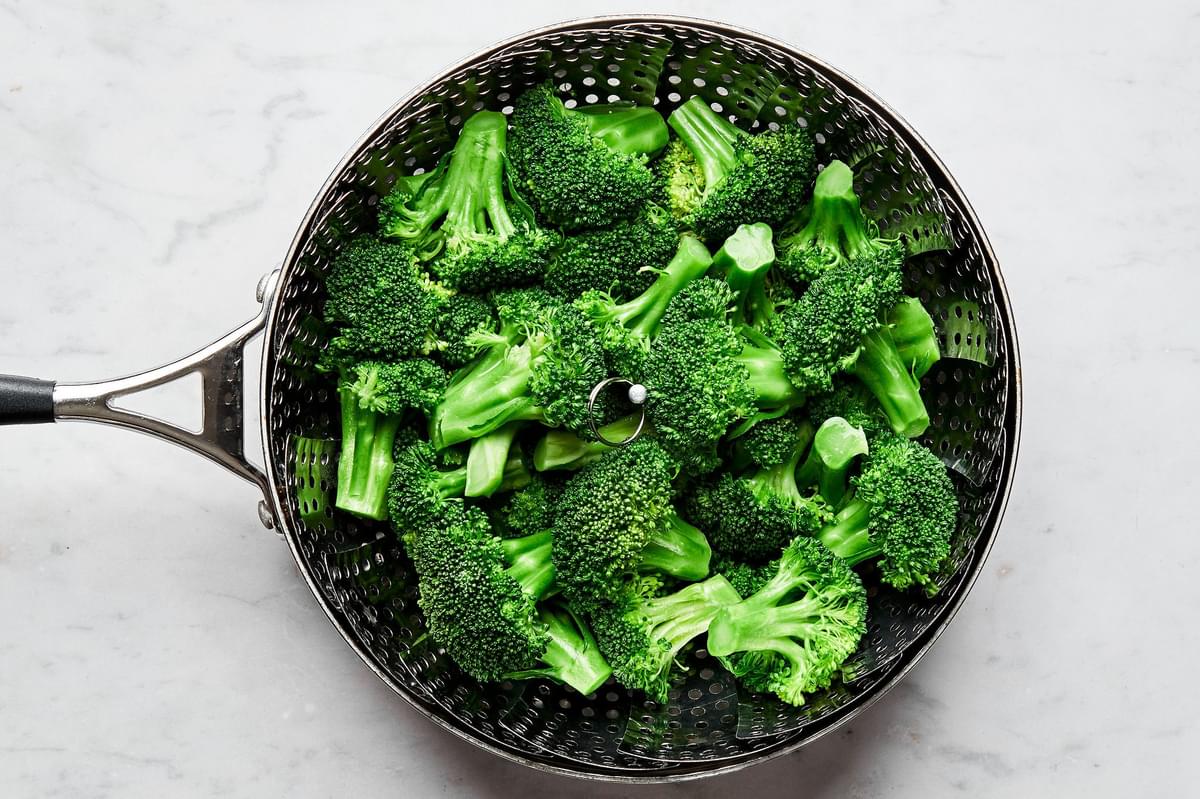 broccoli being steamed in a pot of salted water with a steamer basket set inside