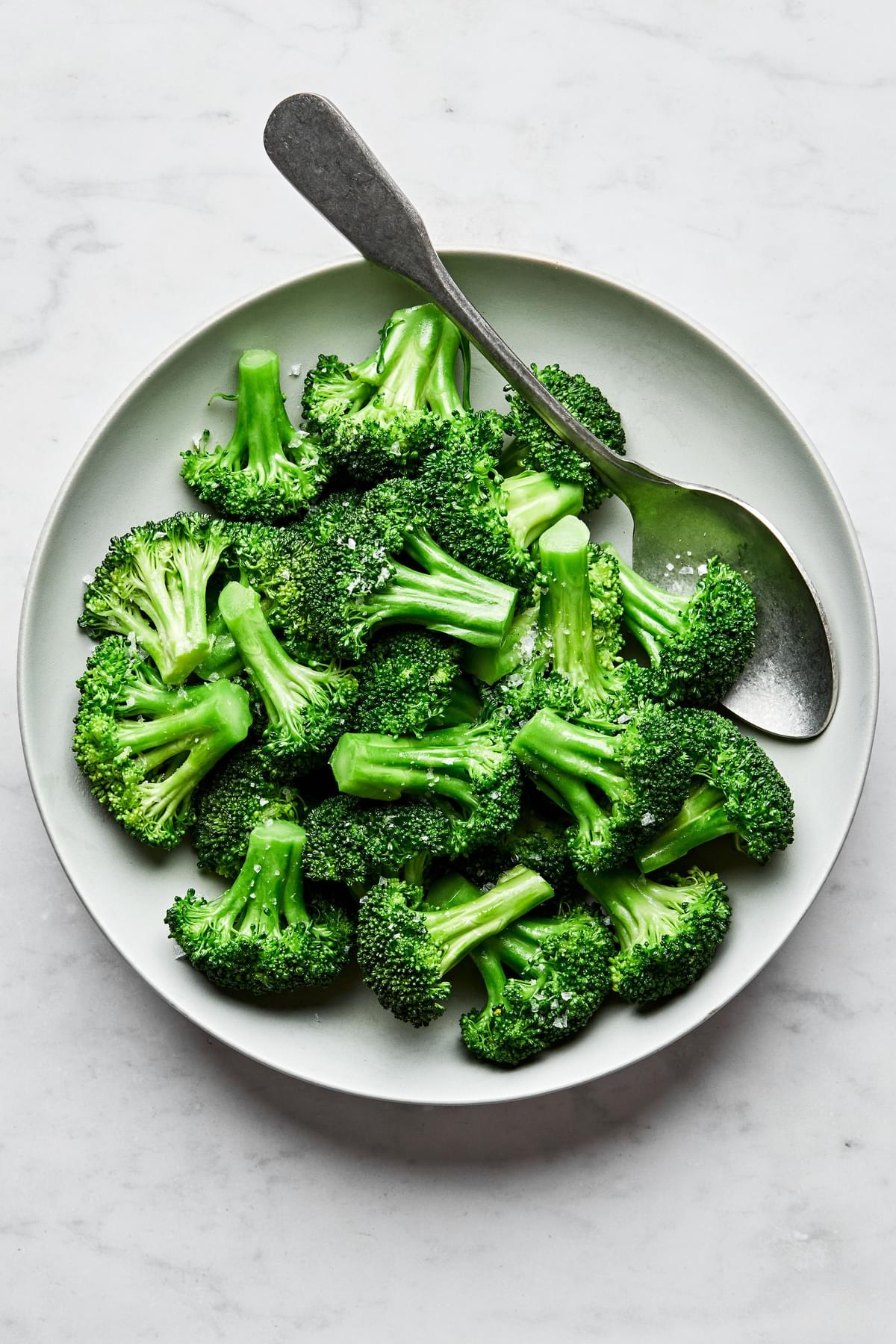 homemade steamed broccoli seasoned with salt in a serving bowl with a spoon