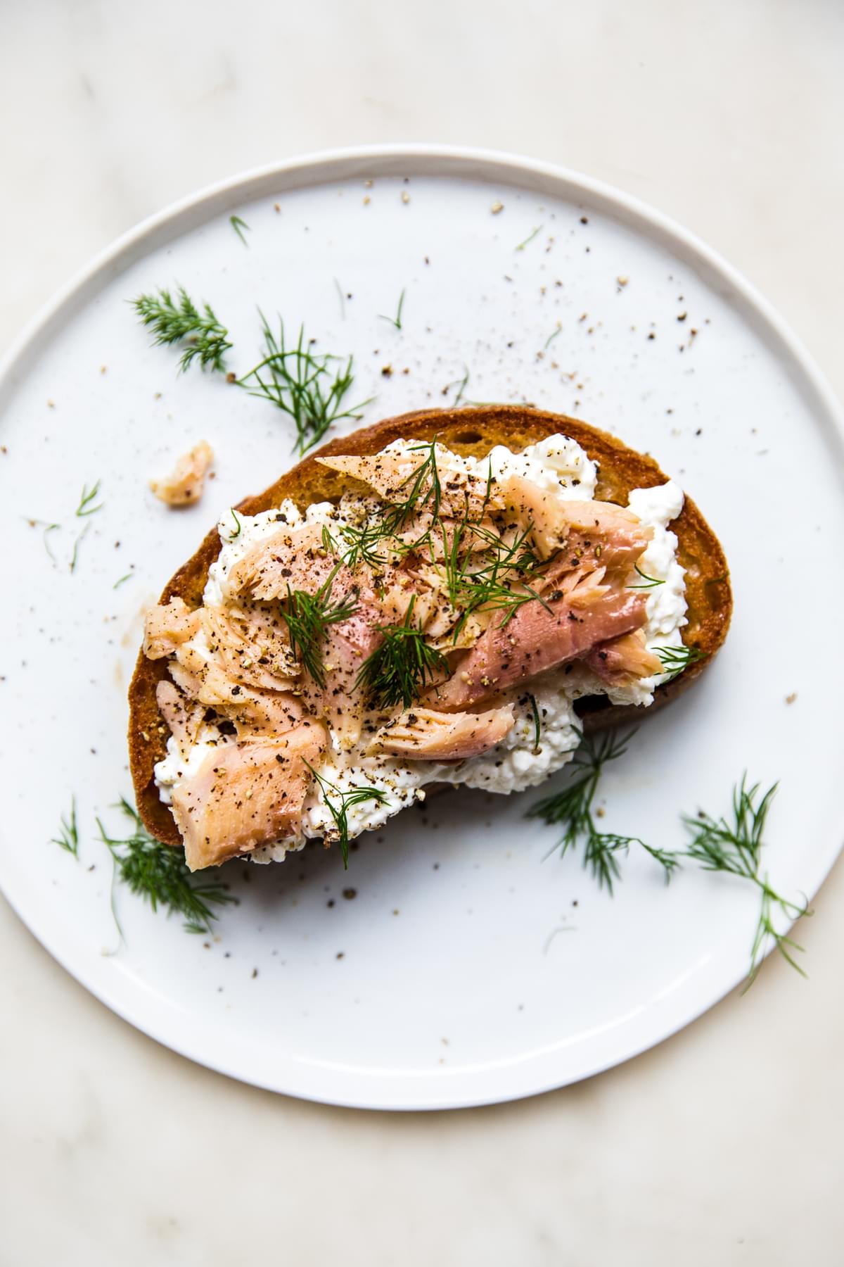 smoked trout on a piece of toast topped  and cottage cheese with fresh dill and cracked pepper