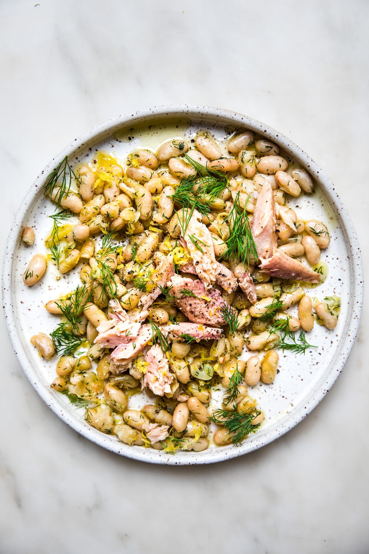 Plate of white beans topped with fresh dill and smoked trout