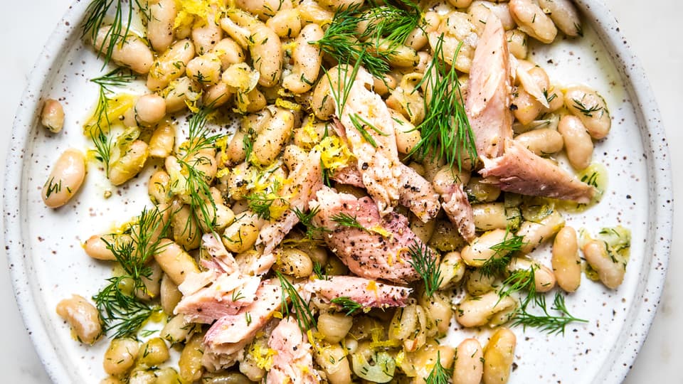 Plate of white beans topped with fresh dill and smoked trout